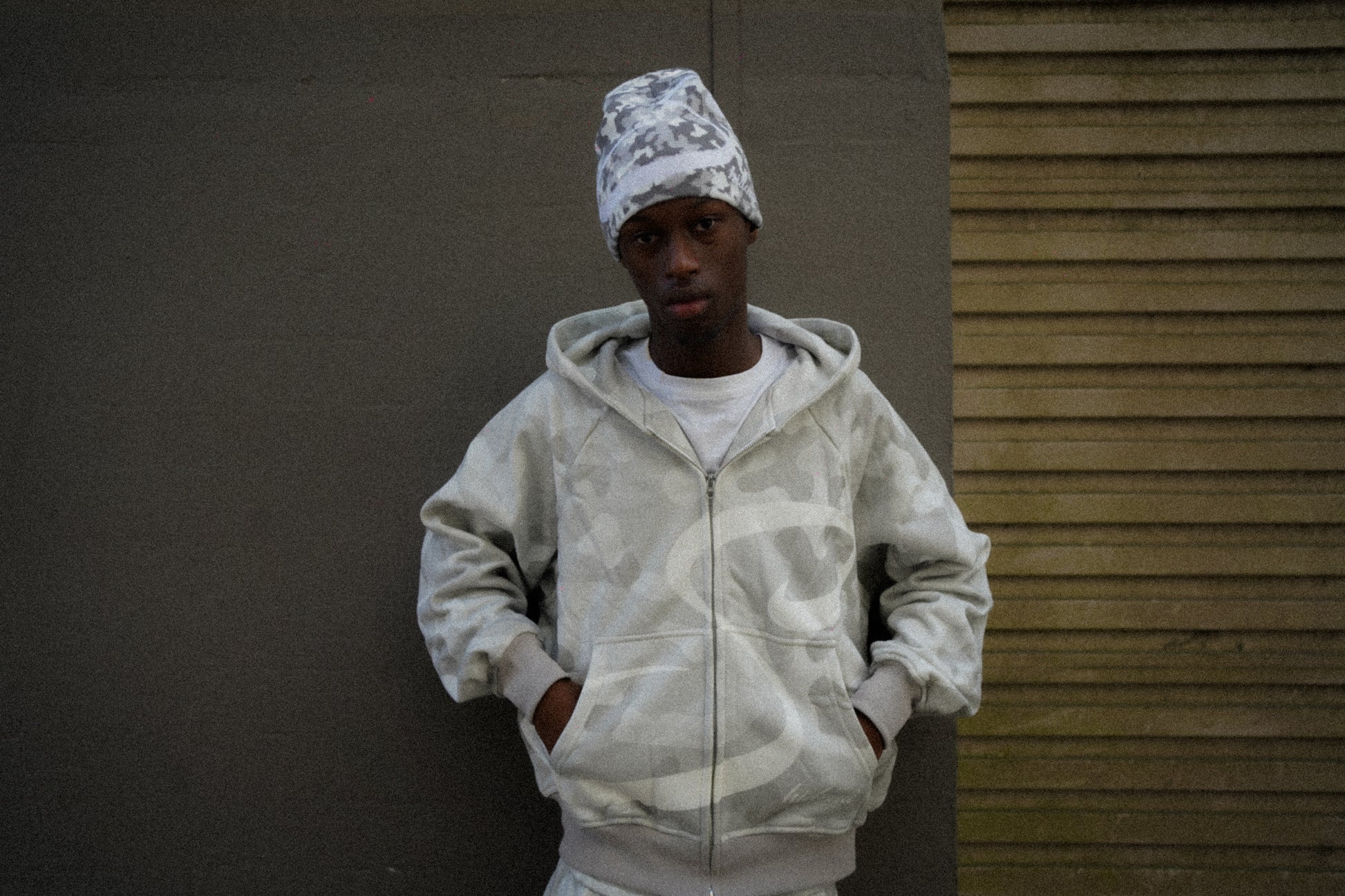 Person wearing a camouflage hoodie and beanie against a plain background