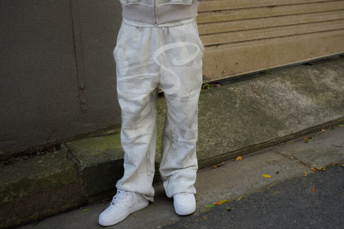Person wearing a camouflage tracksuit standing on a sidewalk.