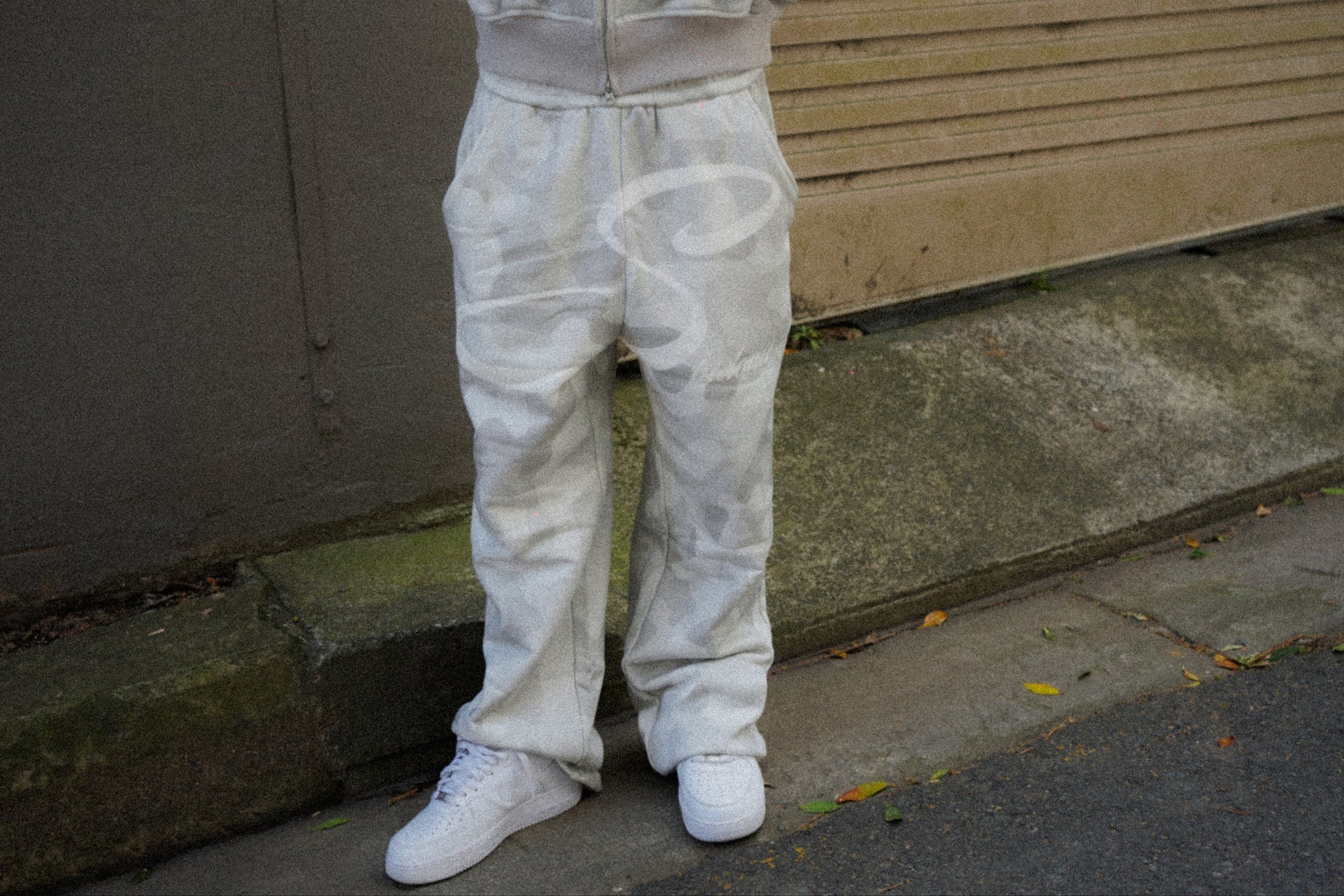 Person wearing a camouflage tracksuit standing on a sidewalk.