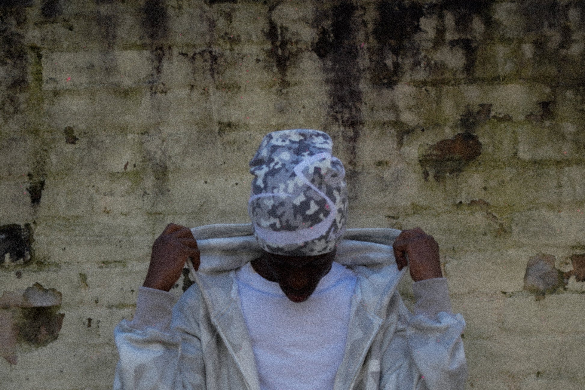 Person wearing a light-colored outfit against a textured wall